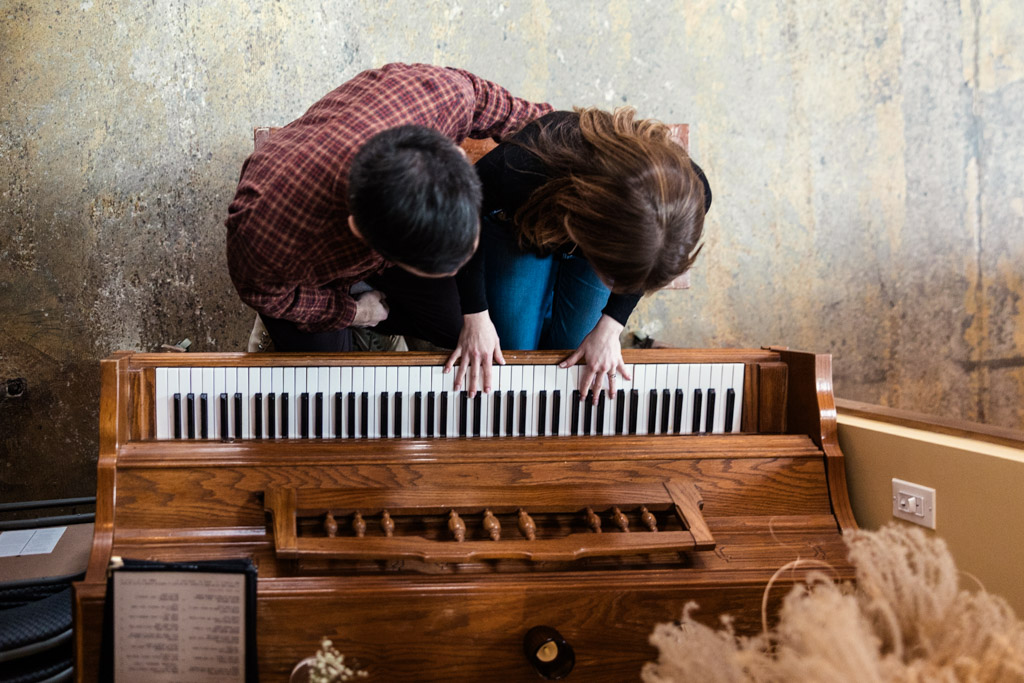 Overhead view of woman playing a wooden piano while her partner sits next to her during a cozy Chicago winter engagement session