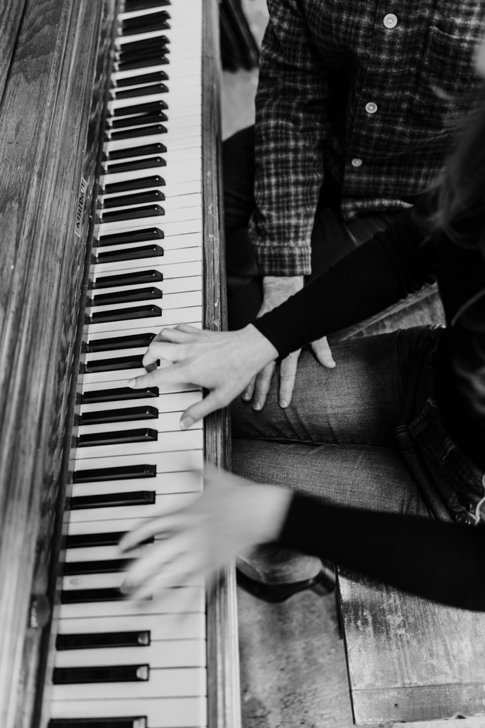 Black and white photo of a woman playing the piano while her partner sits next to her during their Chicago winter engagement session