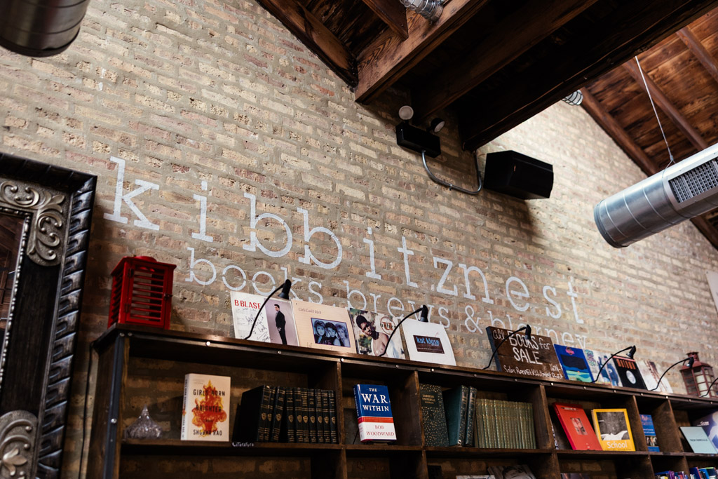 Painted logo on a brick wall at Kibbitznest with books and art displayed on shelves beneath