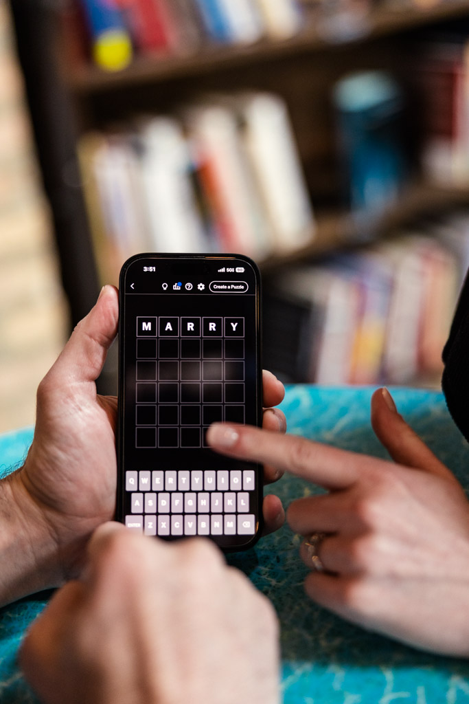 Two people play a word game on a phone during their Chicago winter engagement session; the word 