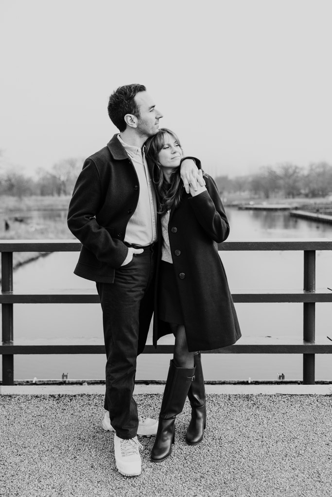 Black and white photo of engaged couple on a bridge over a Lincoln Park pond on a foggy winter day