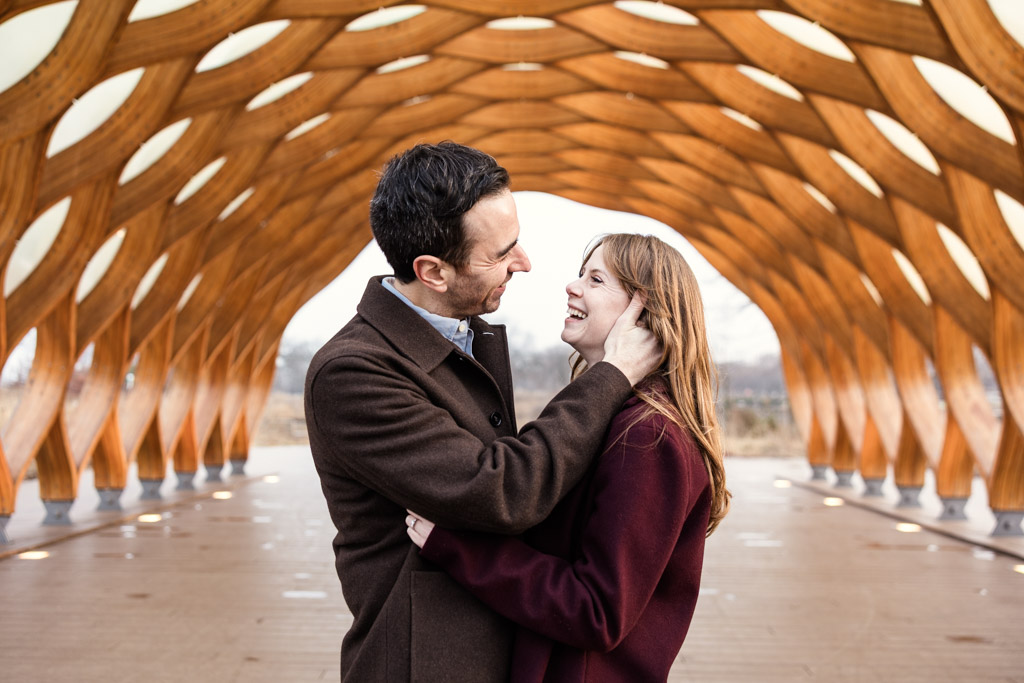 A couple smiles and embraces under the Lincoln Park Honeycomb during their Chicago winter engagement session