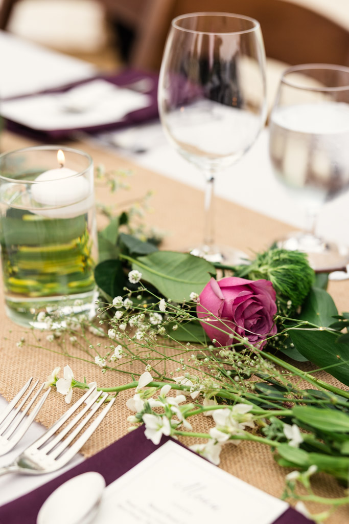 A purple rose, greenery, and a floating candle decorate a guest table for Terra Mia Vineyard wedding reception