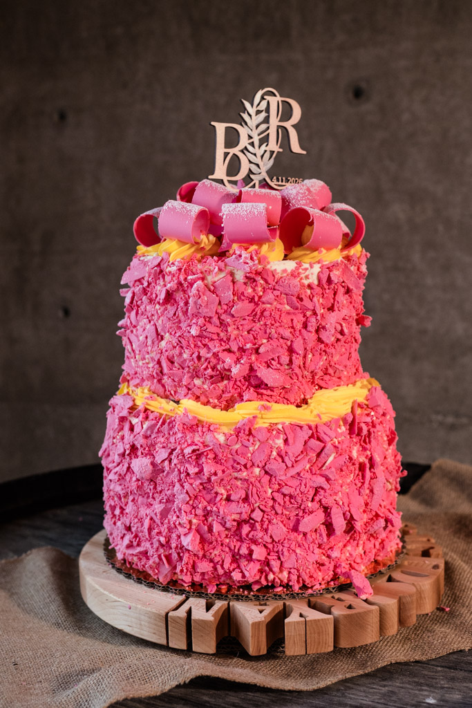 Two-tier pink cake with yellow frosting, pink chocolate curls, and a decorative 