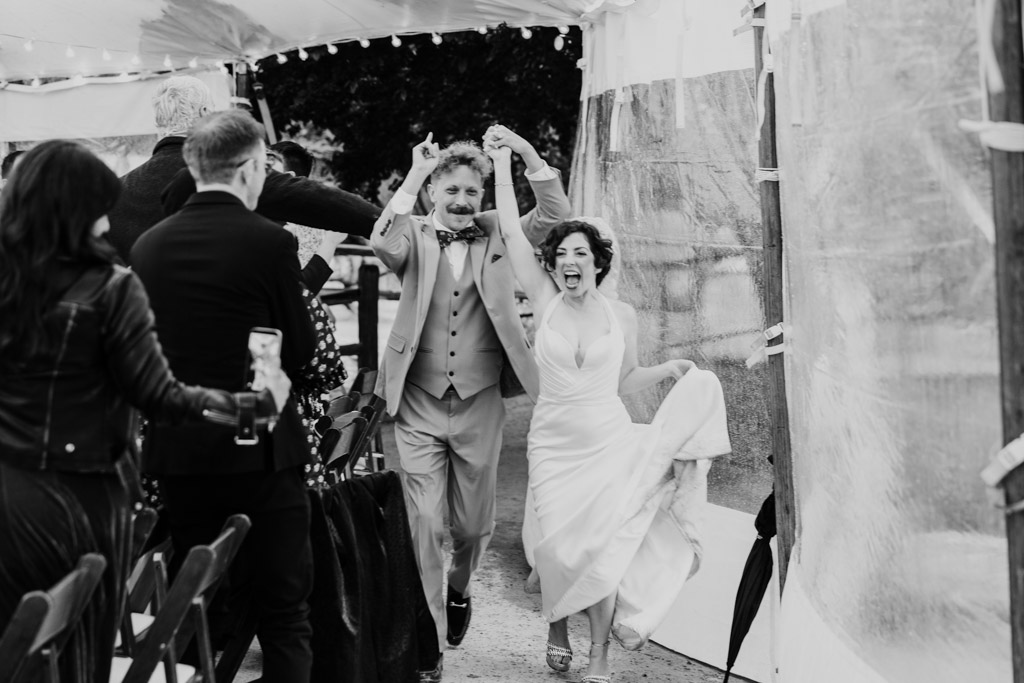 Black and white photo of happy newlyweds entering their Terra Mia Vineyard wedding reception, guests cheering around them