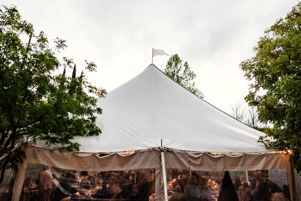 A large white event tent with people inside, surrounded by trees and lit with string lights at dusk for wedding reception at Terra Mia Vineyard