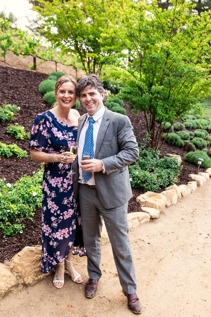 A smiling couple dressed formally stands outdoors on a garden path during Terra Mia Vineyard wedding reception