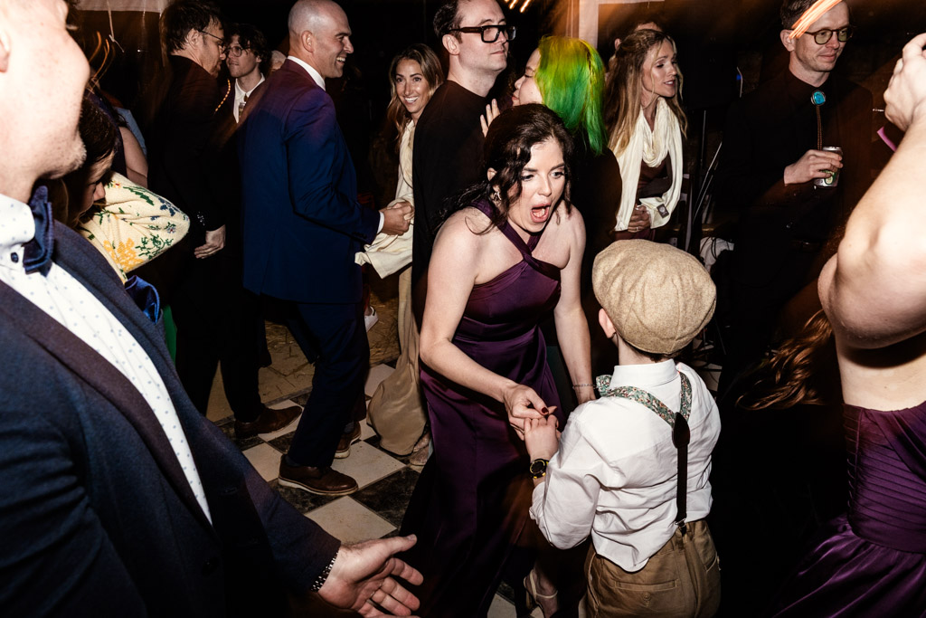 Bridesmaid in a purple dress dances with a young boy in suspenders and cap during wedding reception at Terra Mia Vineyard