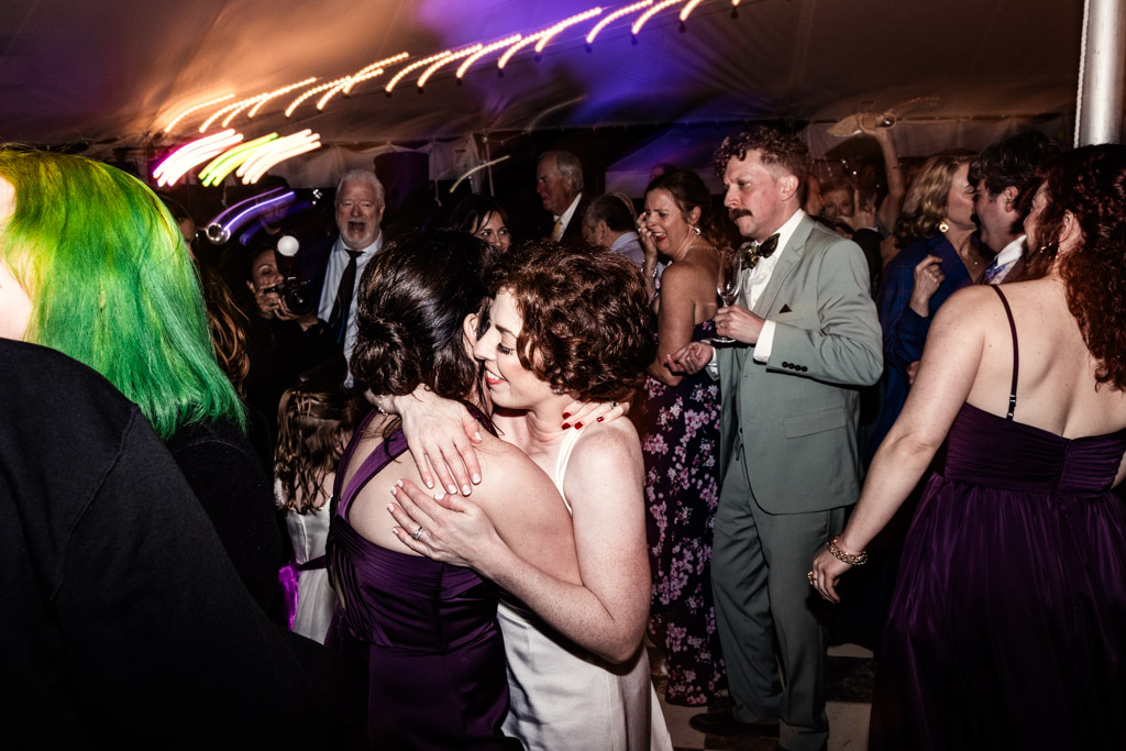 Bride and her sister embrace on a crowded, colorful dance floor during wedding reception at Terra Mia Vineyard