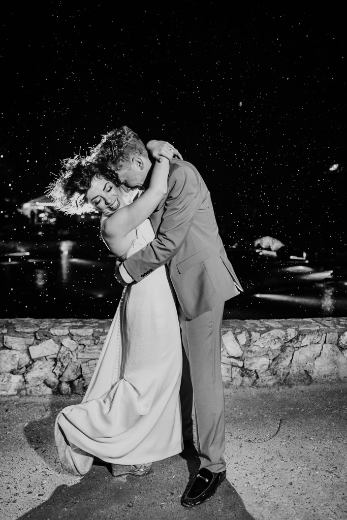 Black and white photo of bride and groom embracing in the rain at night during their wedding reception at Terra Mia Vineyard