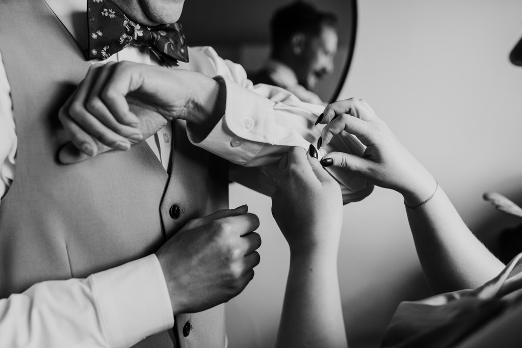 Black and white photo of Maid of Honor helping groom with his shirt sleeve and cuff in preparation for his Terra Mia Vineyard wedding celebration