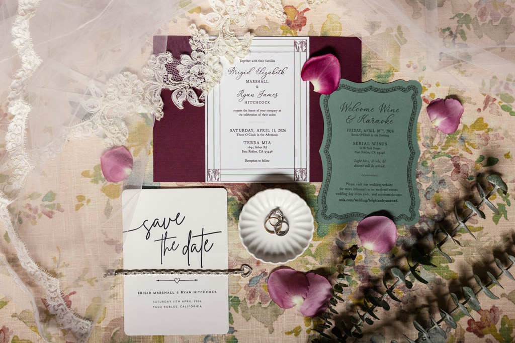Flat lay of wedding invitations, rings in a dish, petals, lace, and a save-the-date card for Terra Mia Vineyard wedding in Paso Robles, California