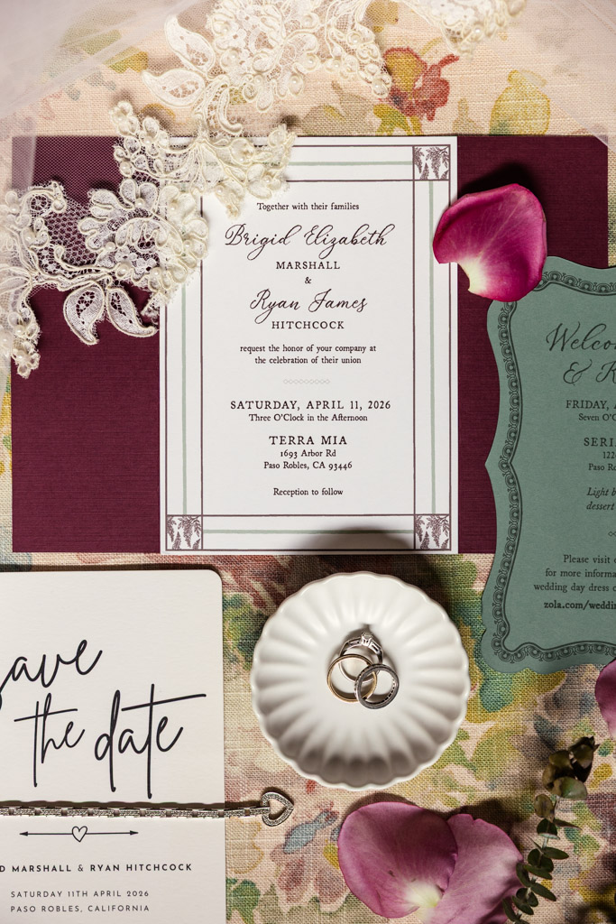 Wedding invitation suite with rings in a dish, lace, petals, and save the date card arranged on floral fabric for Terra Mia Vineyard wedding in Paso Robles, California
