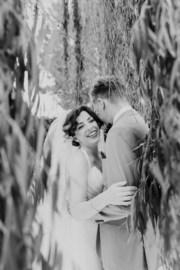 Black and white photo of bride and groom embracing under hanging tree branches at Terra Mia Vineyard