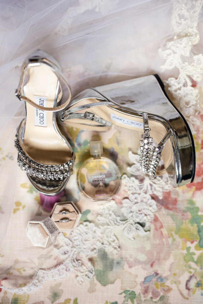Bride's silver Jimmy Choo heels, Chanel perfume, veil and rings rest on floral fabric for Terra Mia Vineyard wedding celebration