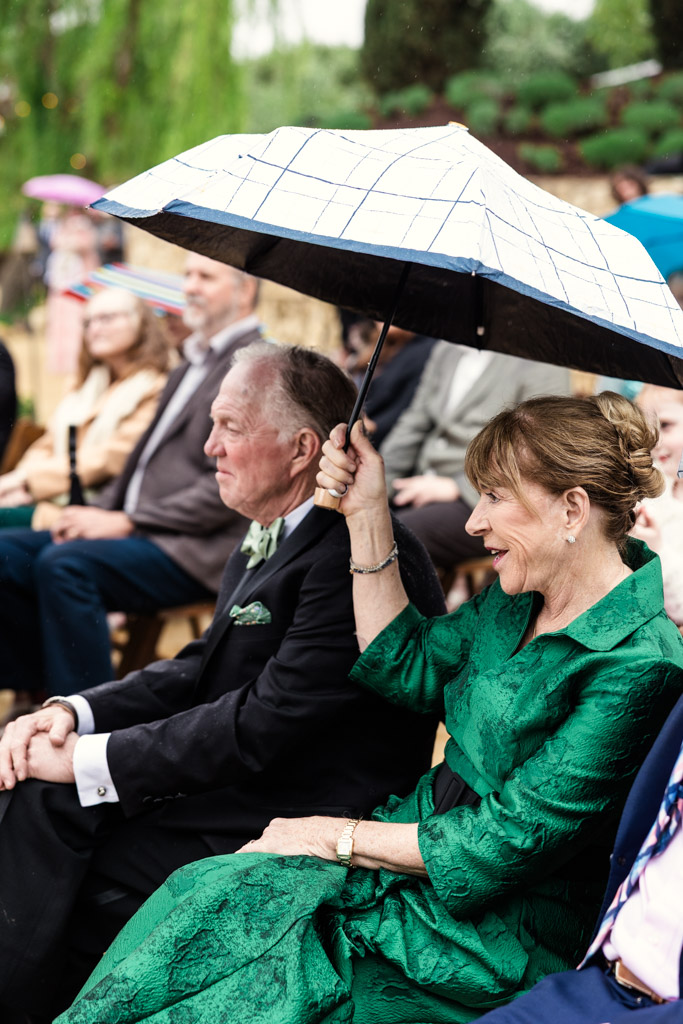 Mother of the bride in a green dress holds an umbrella over herself andher husband during Terra Mia Vineyard wedding