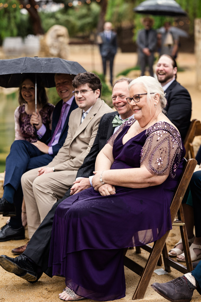 Groom's parents smile and sit outdoors on wooden chairs during wedding ceremony at Terra Mia Vineyard