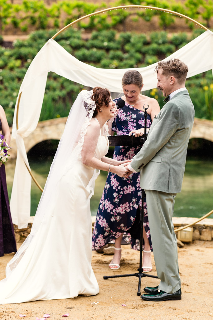 Bride and groom holding hands and smiling during a beautiful Terra Mia vineyard wedding ceremony with the officiant behind them.