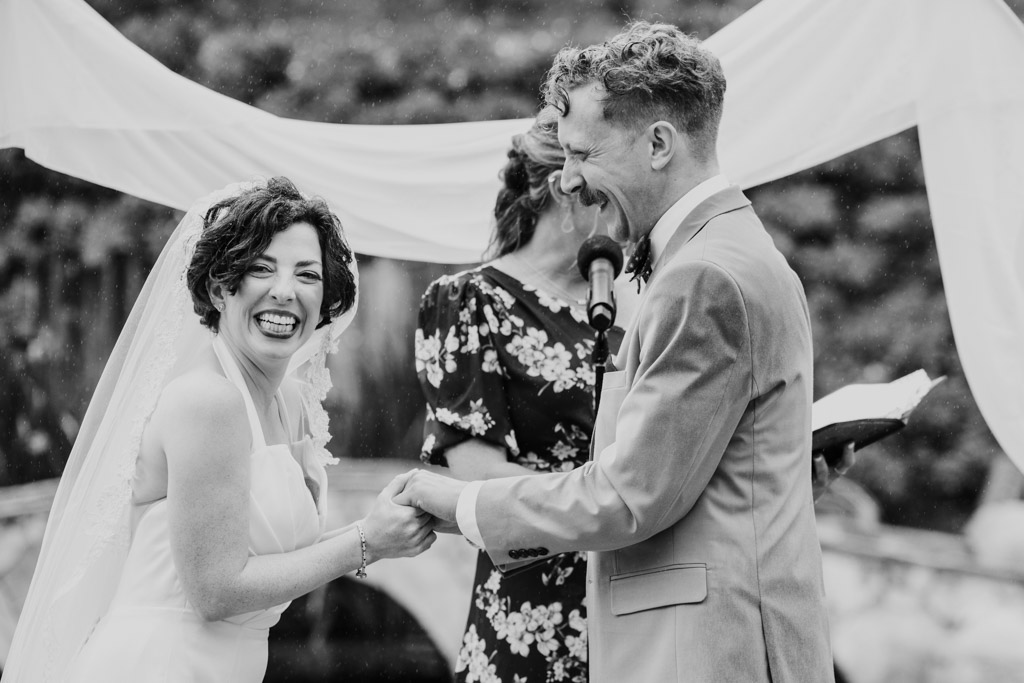 Black and white photo of bride and groom laughing and holding hands during their outdoor wedding ceremony at Terra Mia Vineyard in Paso Robles, California