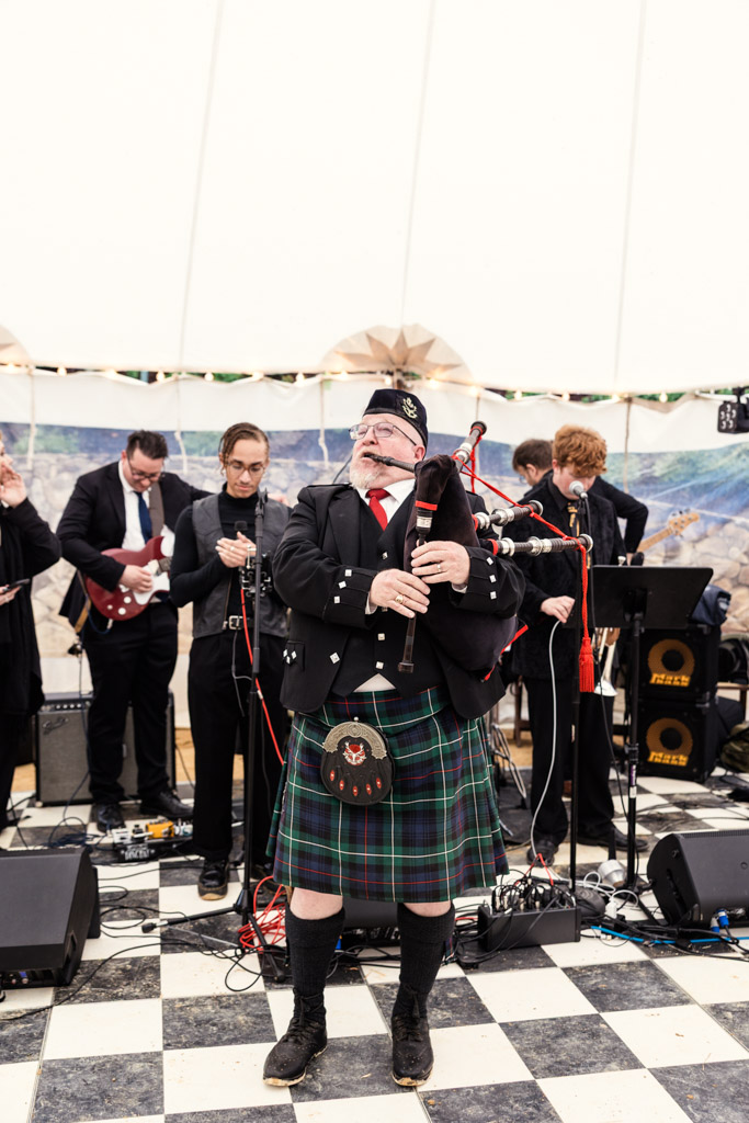 A man in a kilt plays bagpipes with a band on a checkered floor under a white tent at Terra Mia Vineyard wedding reception