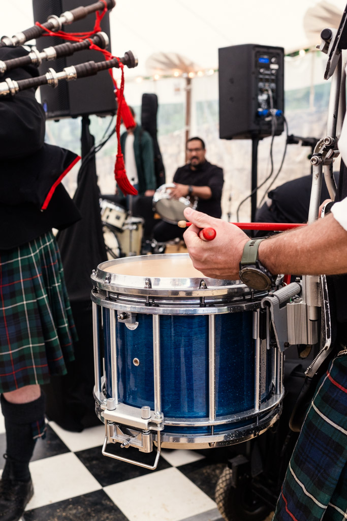 Person playing a snare drum with drumsticks, surrounded by musicians in kilts at Terra Mia Vineyard wedding reception