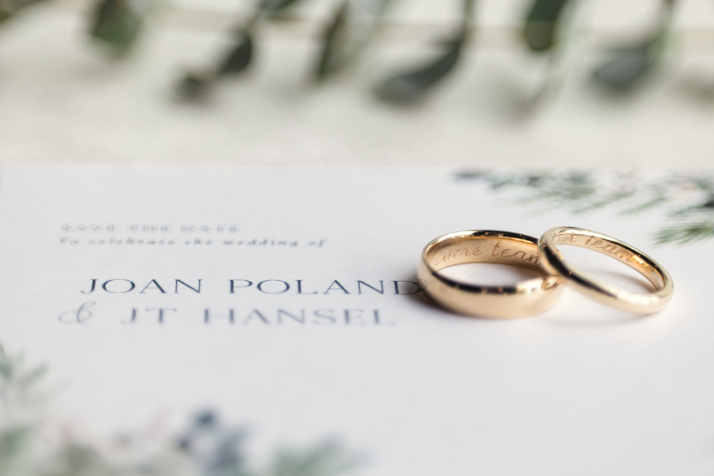 Two gold wedding rings resting on a wedding invitation with blurred greenery in the background, capturing the elegant charm of a Bottom Lounge wedding.