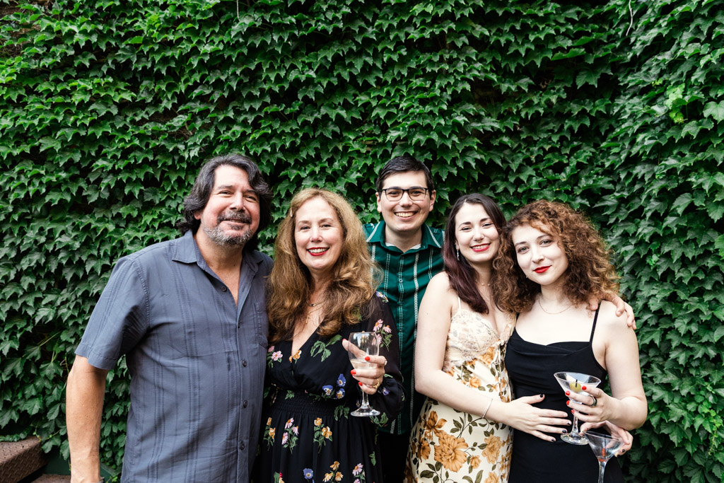 Guests smiling and posing together in front of a leafy green wall at Firehouse Chicago wedding reception holding drinks
