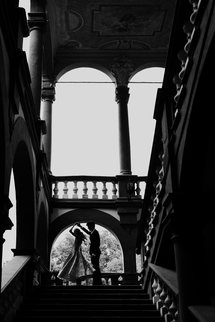 Black and white silhouette of a couple dancing on a grand staircase under archways in a historic building in Lucca, Italy