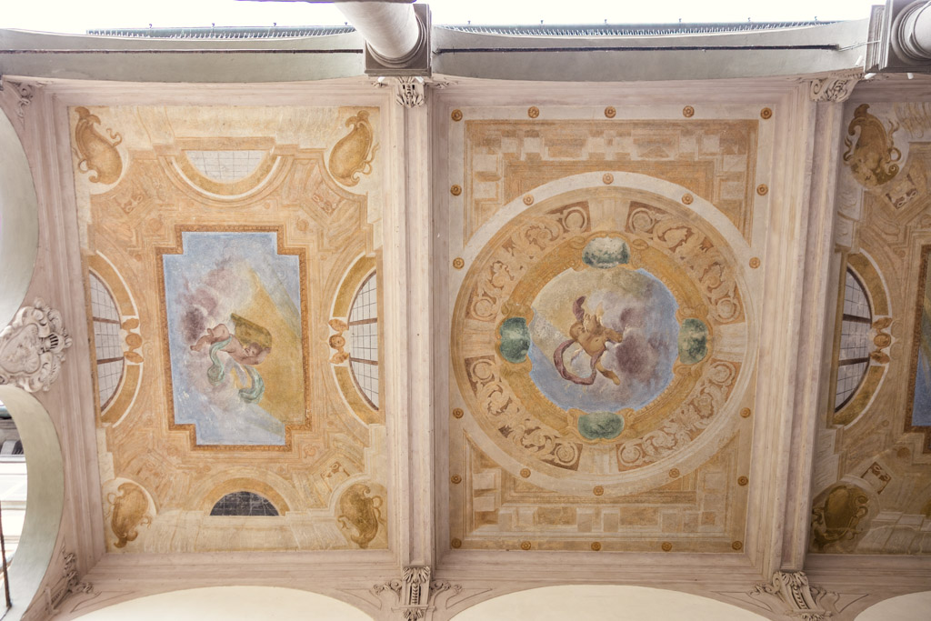 Painted ceiling with classical frescoes and ornate details, featuring angels and decorative motifs in soft colors on a building in Lucca, Italy