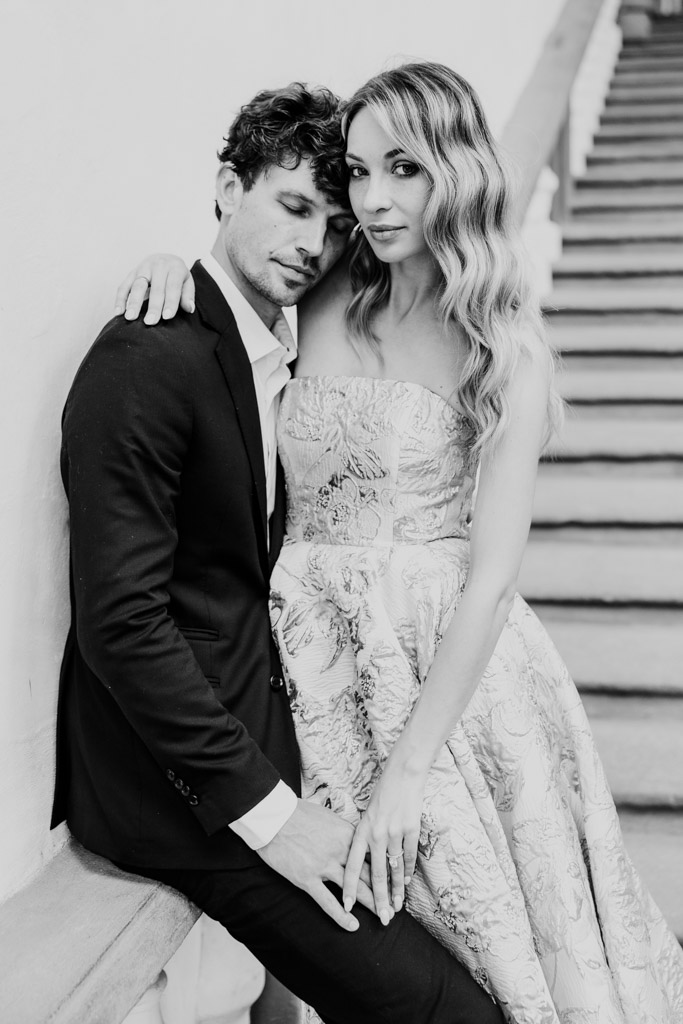 Black and white portrait of couple on a staircase during their Lucca engagement session, the woman in a strapless dress and the man in a suit