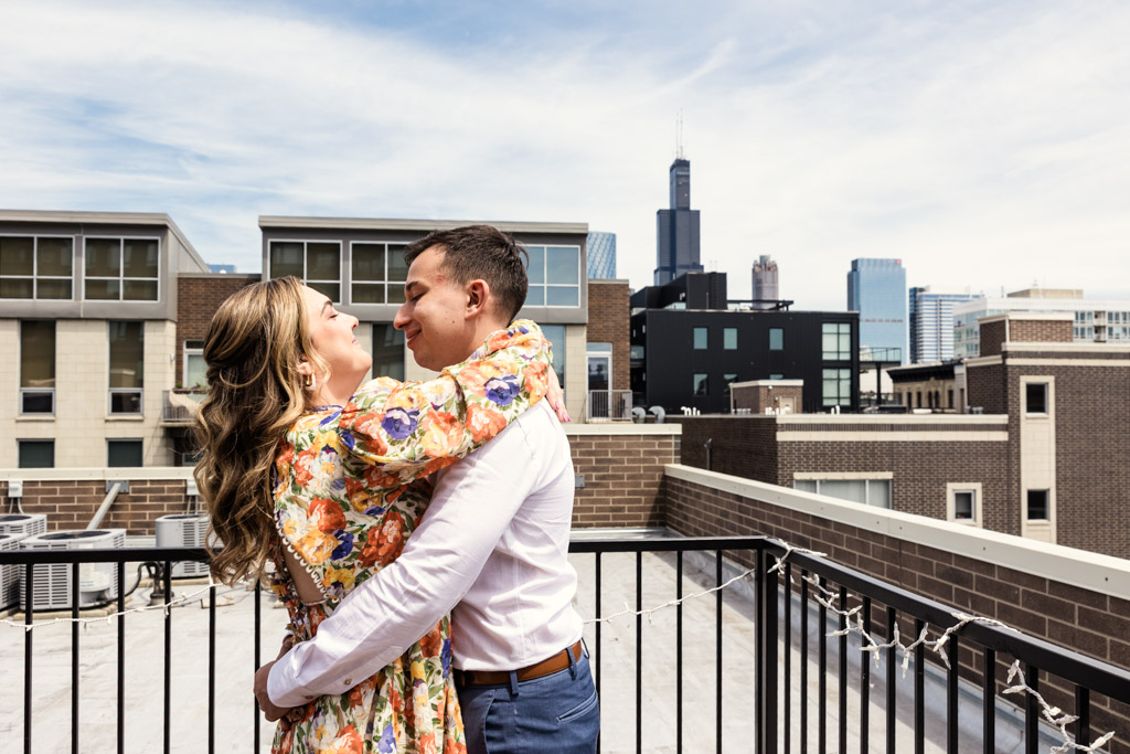 Engaged couple embraces on a rooftop with Chicago skyline and skyscrapers in the background during their summer engagement session