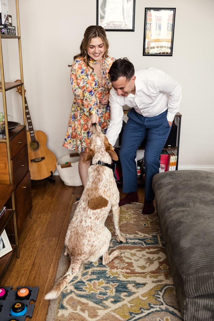 Happy couple pets their dog in their living room during their summer engagement session