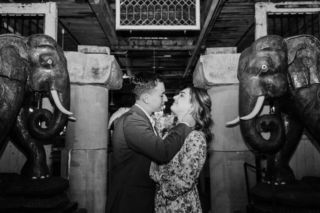 Black and white photo of couple embracing and smiling at each other between two large elephant statues during their Salvage One engagement session