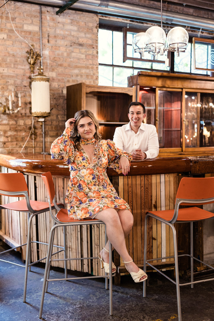 At Salvage One, a woman in a floral dress sits at the bar while a man in a white shirt stands behind the counter, both smiling