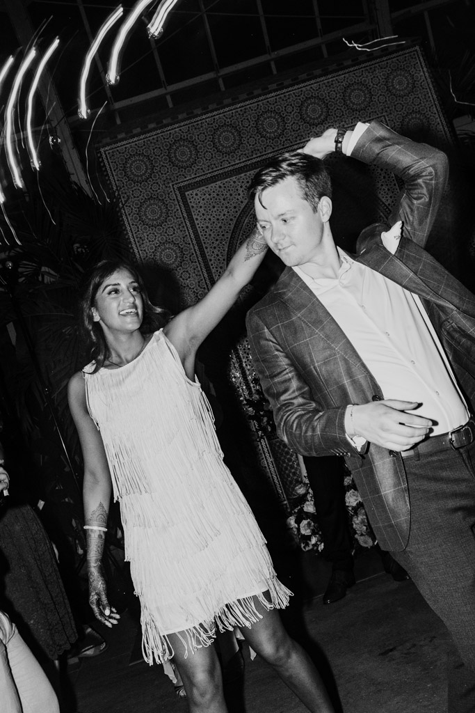 Black and white photo of happy newlywed couple dancing together at night, with the bride spinning under the groom's raised arm