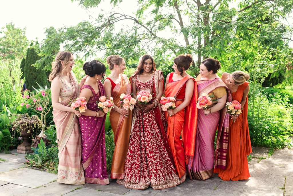bride ad bridesmaids in colorful sarees and gowns, holding bouquets, stand smiling inside Garfield Park Conservatory