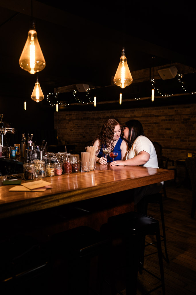 Engaged couple sits at the bar inside Clara in Wicker Park under warm hanging lights and string lights