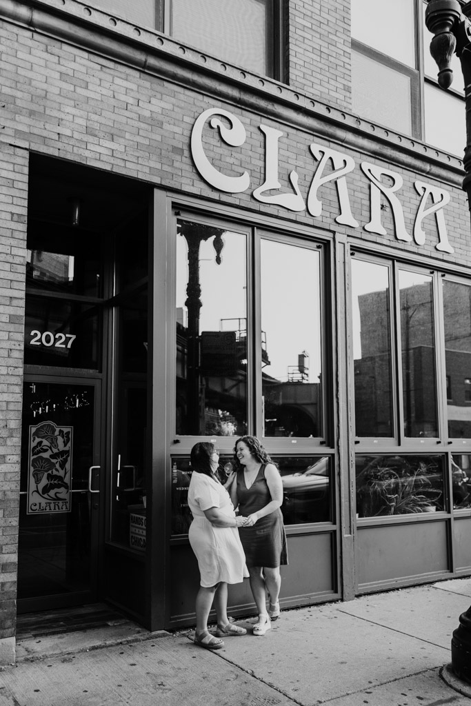 Black and white photo of engaged couple standing outside Clara cocktail bar in Wicker Park