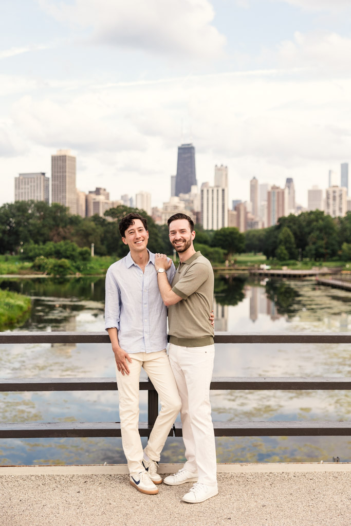Portrait of happy engaged couple standing together on a Lincoln Park bridge with city skyline and water in the background during their Chicago lakefront engagement session