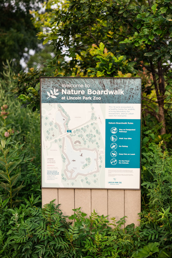 Sign for Nature Boardwalk at Lincoln Park Zoo with a map and list of rules, surrounded by greenery