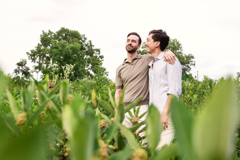 Two men stand together in a green field in Lincoln Park, smiling with arms around each other on a cloudy day