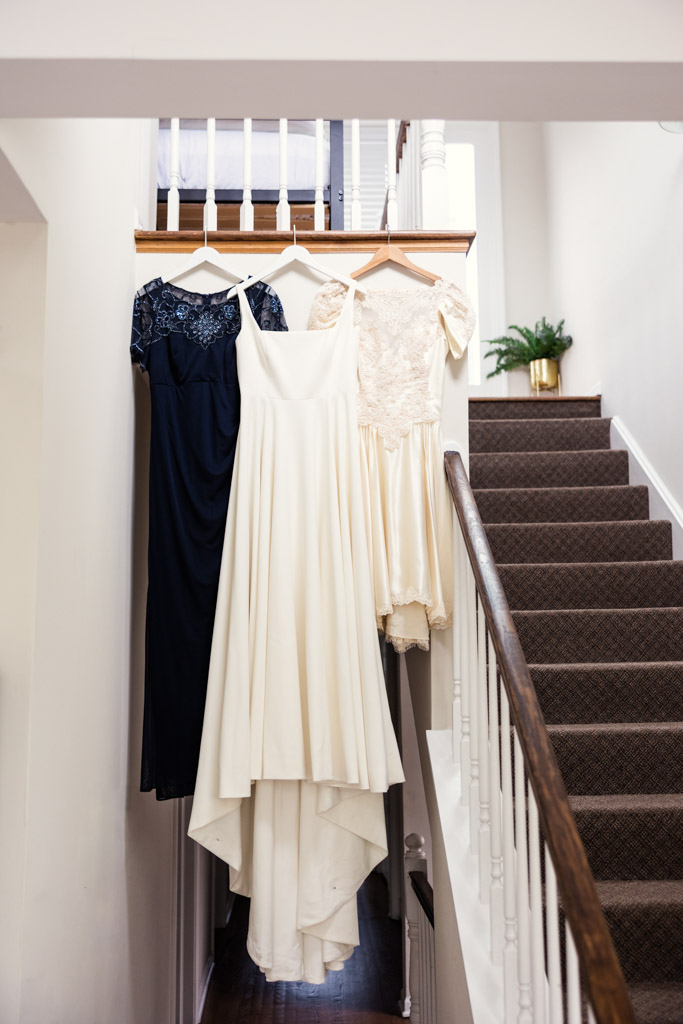 Three dresses—navy, white, and cream—hang on hangers at the top of a staircase in the The Library at Hotel Lincolm=n