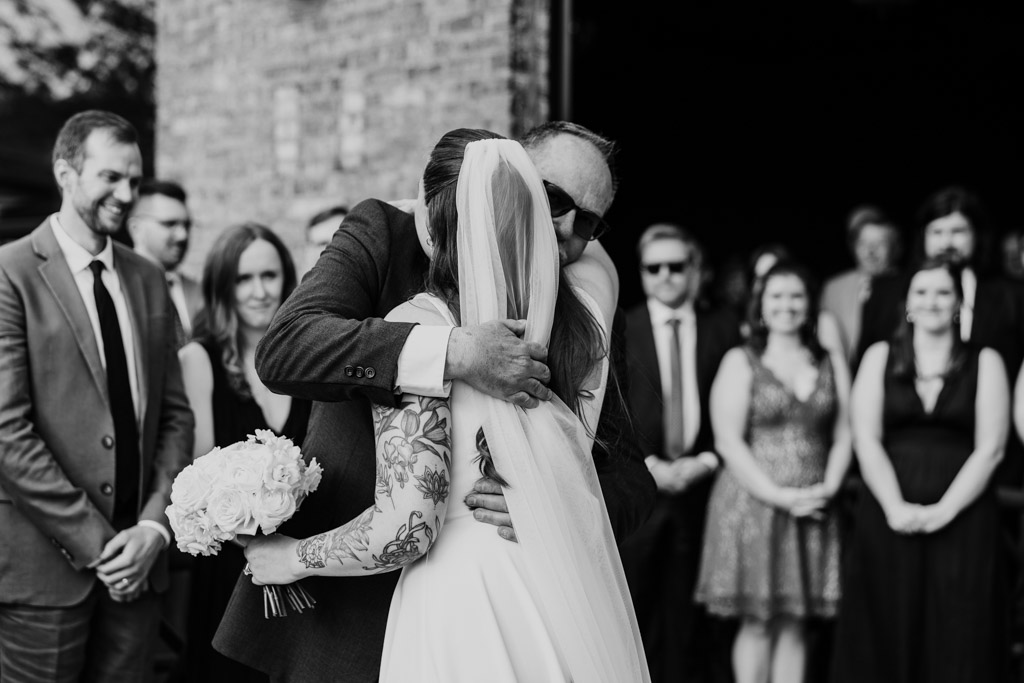 A bride hugs her father as guests watch at her River Room wedding ceremony