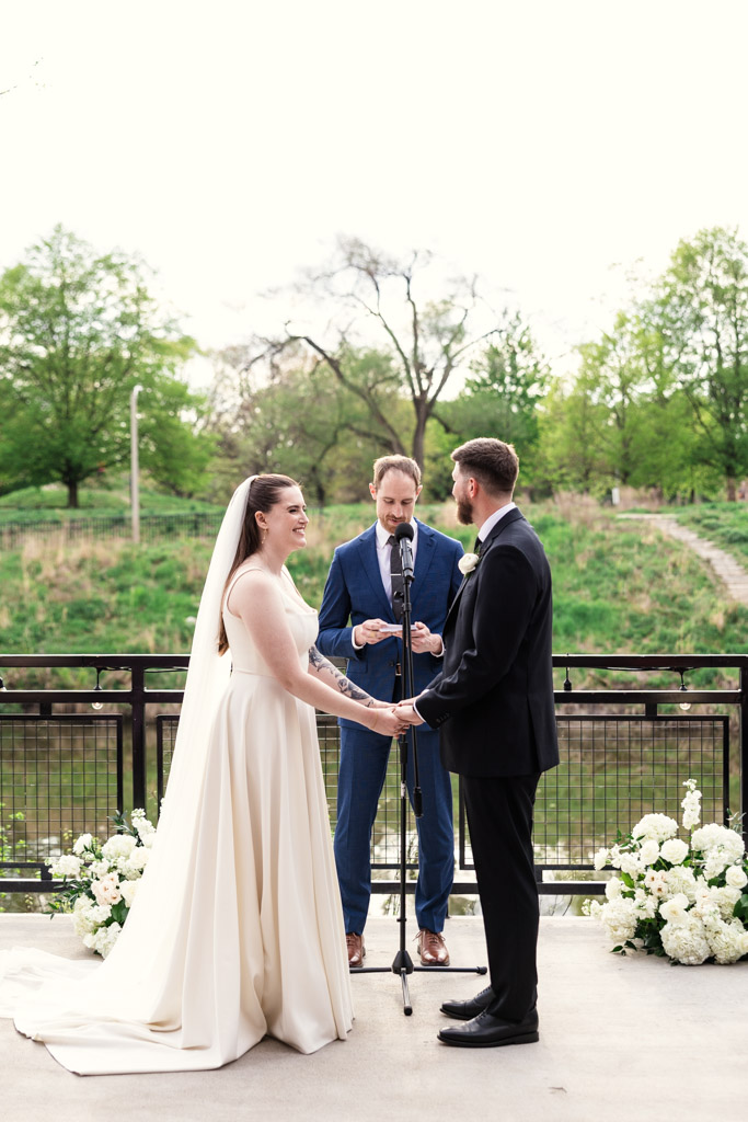 A bride and groom hold hands during their outdoor River Room wedding ceremony with an officiant between them