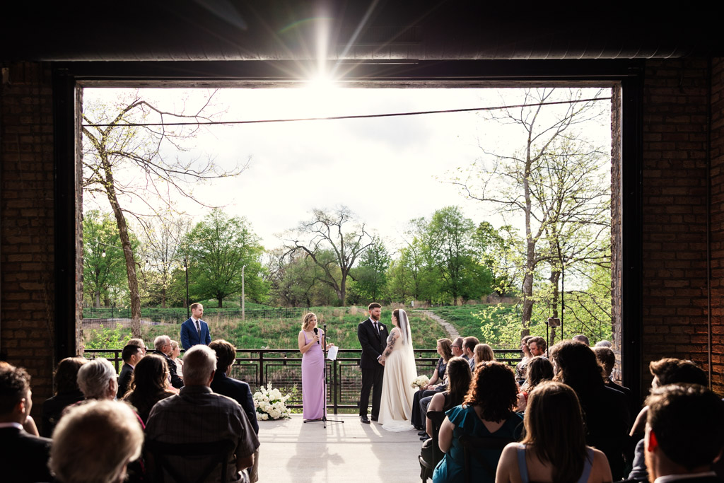 A wedding ceremony takes place on the River Room patio with sunlight streaming in through a large open doorway
