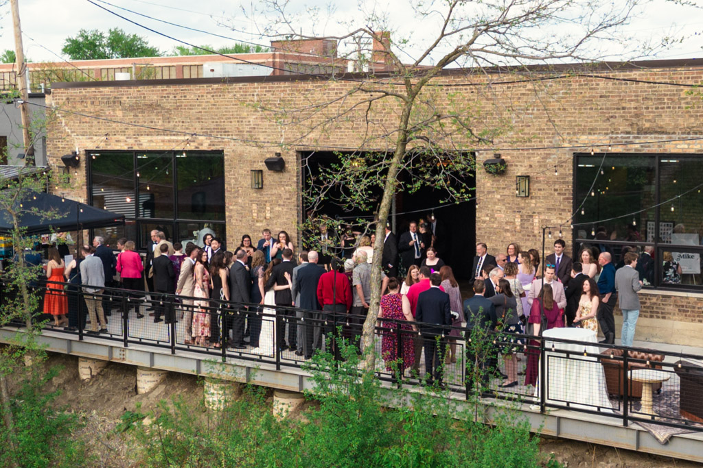 Guests in formal attire gather outside on the River Room patio during cocktail hour