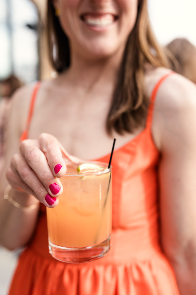 Woman in orange dress holding a custom cocktail with a lime slice and black straw for wedding reception at River Room