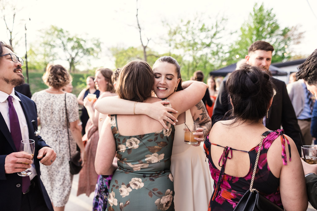 Bride hugs a guest during cocktail hour at River Room, surrounded by other guests dressed in formal attire