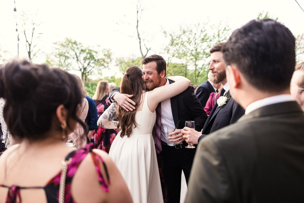 Bride hugs a man in a suit during her River Room wedding reception with other guests nearby