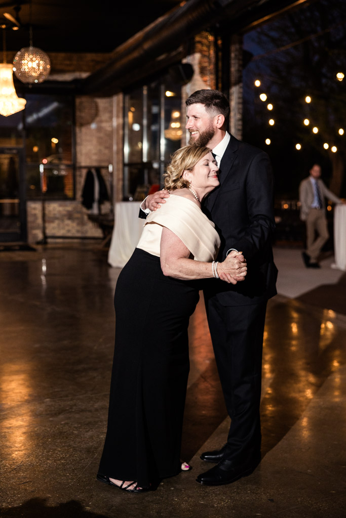 Groom and his mother dance together during wedding reception in the River Room, smiling and embracing closely
